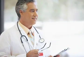 A doctor is holding his stethoscope and looking at the camera.