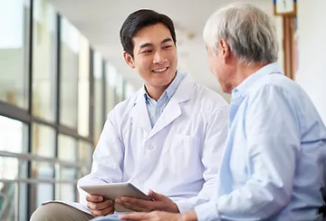 A man in lab coat holding a tablet and talking to another man.