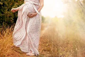 A pregnant woman in a long dress standing on the side of a road.